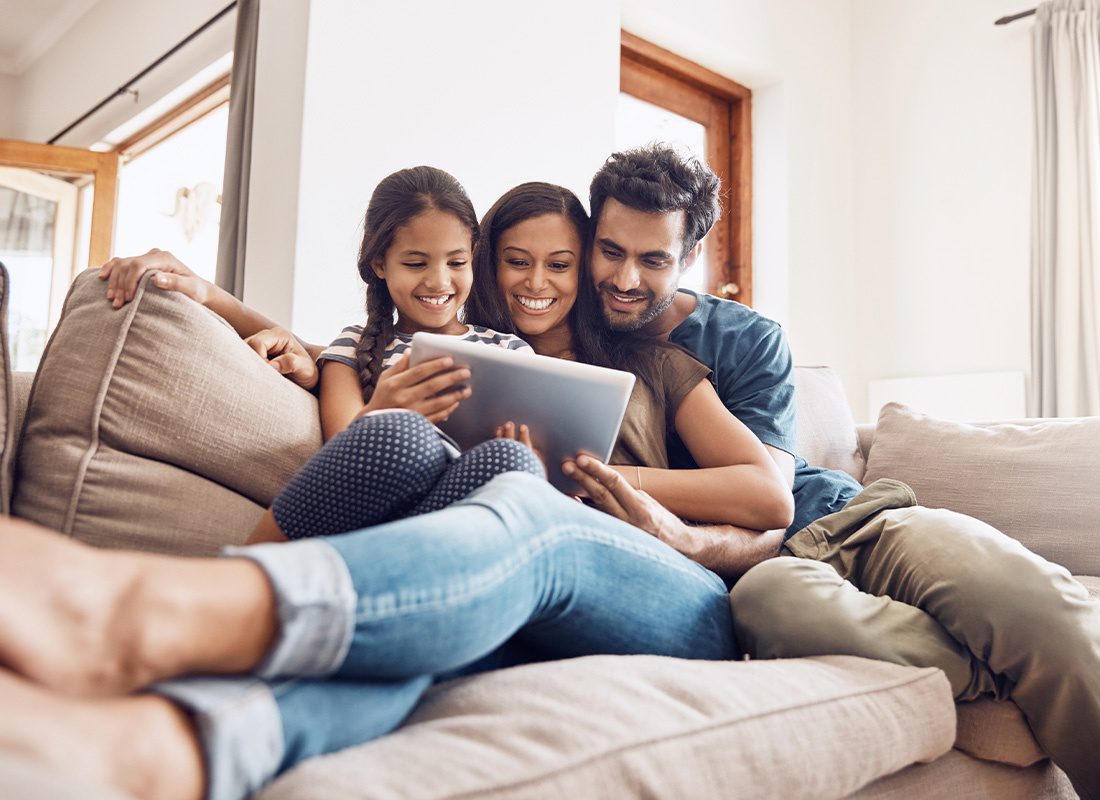 Service Center - Mother and Father Using a Digital Tablet With Their Daughter on the Sofa at Home